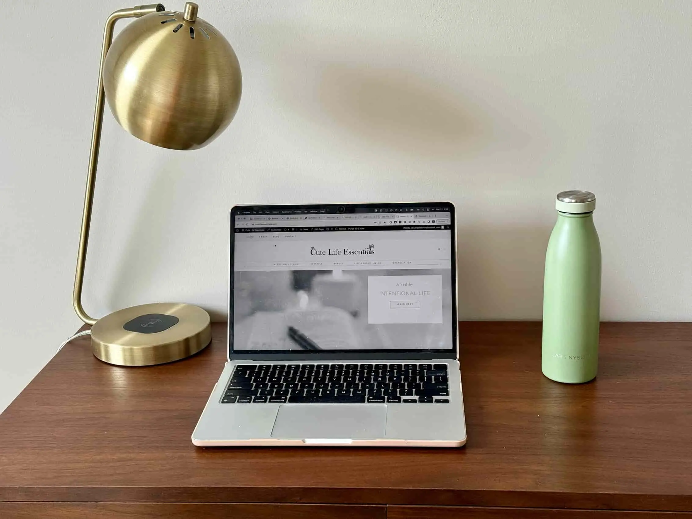 A desk with a gold lamp , a laptop and a water bottle 